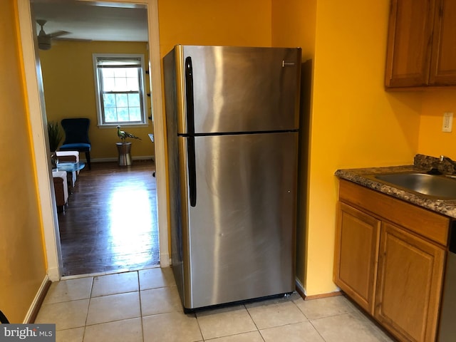 kitchen with freestanding refrigerator, a sink, brown cabinetry, and baseboards