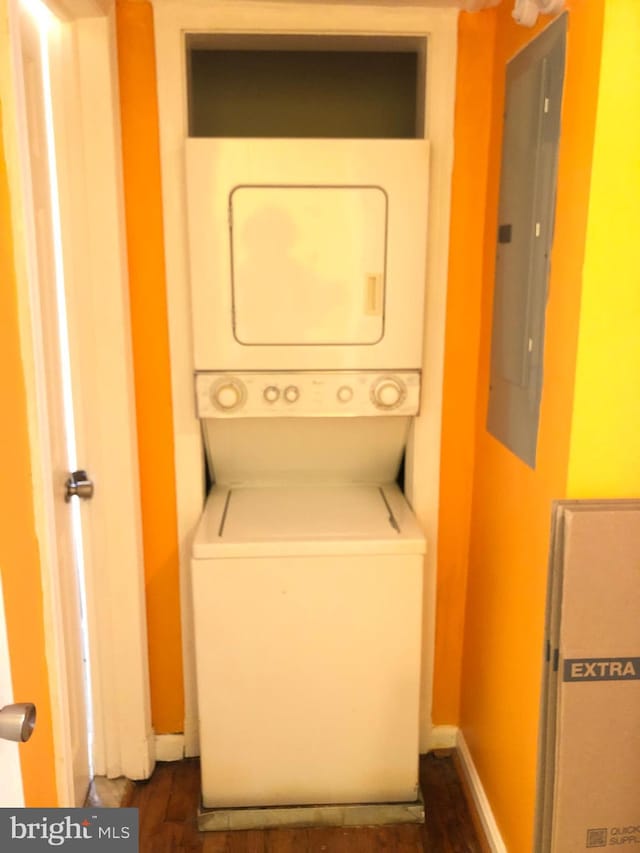 clothes washing area featuring stacked washing machine and dryer, electric panel, baseboards, and dark wood-style floors