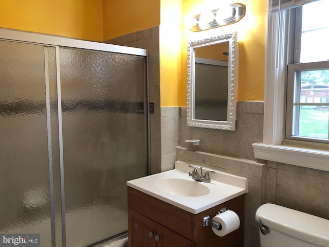 bathroom featuring tile walls, a shower stall, toilet, vanity, and wainscoting