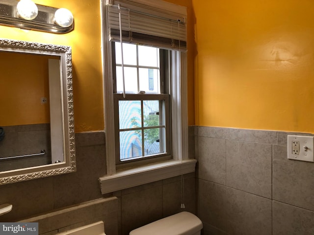 half bath with tile walls, toilet, and a wainscoted wall