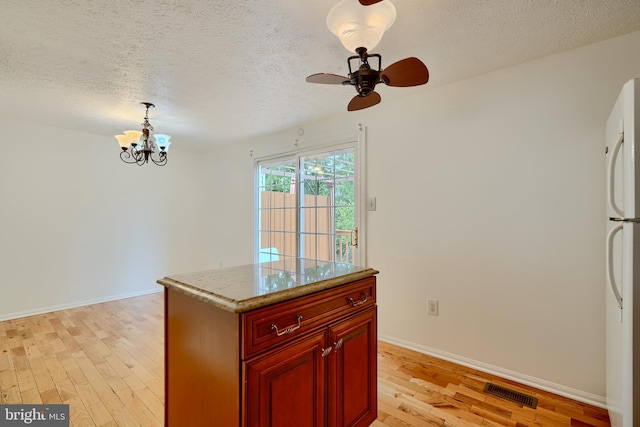 kitchen with a textured ceiling, light wood finished floors, reddish brown cabinets, a chandelier, and freestanding refrigerator