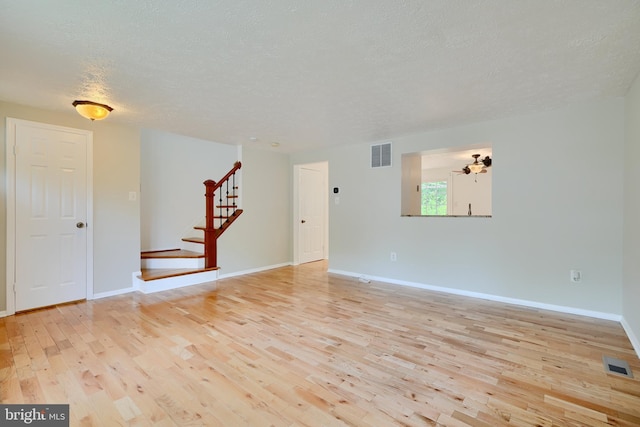 unfurnished living room featuring light wood-style flooring, stairway, a textured ceiling, and baseboards
