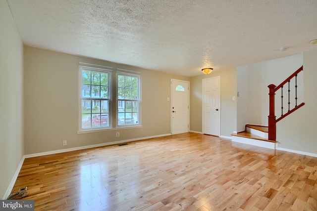 foyer entrance featuring a textured ceiling, light wood-style flooring, stairway, and baseboards