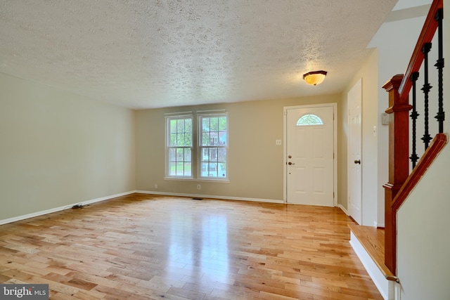 entrance foyer with light wood-style floors, a textured ceiling, stairs, and baseboards