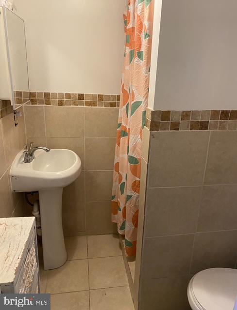 4400 N Franklin St, Philadelphia, PA 19140 - bathroom featuring tile walls, a shower with shower curtain, tile patterned flooring, a wainscoted wall, and toilet