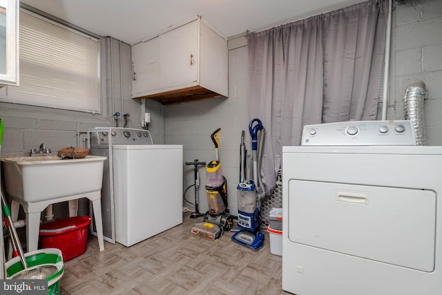 washroom featuring washer and dryer, cabinet space, and concrete block wall