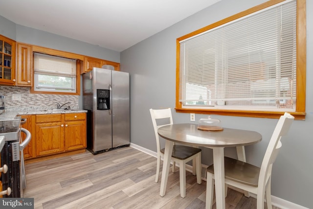 kitchen with stainless steel refrigerator with ice dispenser, a sink, stove, light wood-style flooring, and brown cabinetry