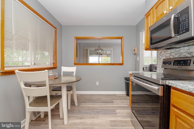 kitchen featuring stainless steel appliances, light wood finished floors, a chandelier, tasteful backsplash, and baseboards