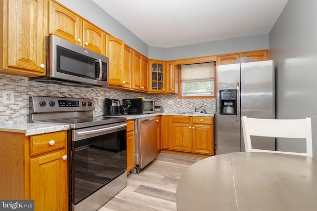 kitchen with appliances with stainless steel finishes, glass insert cabinets, light wood finished floors, a sink, and decorative backsplash