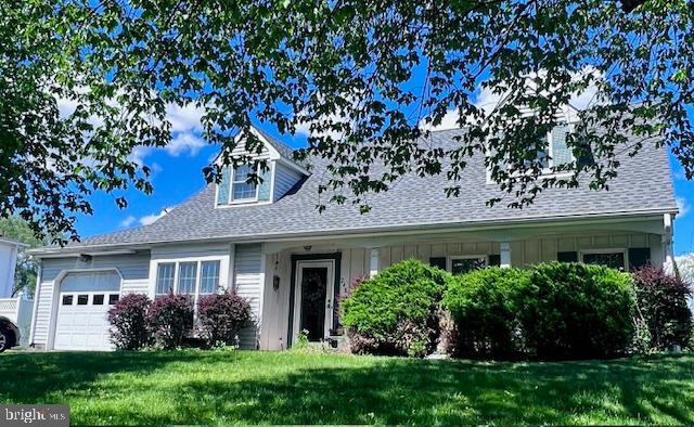 cape cod home with an attached garage, a front lawn, a shingled roof, and board and batten siding