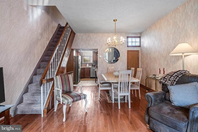 dining room featuring a chandelier, wood finished floors, wallpapered walls, stairway, and a textured ceiling