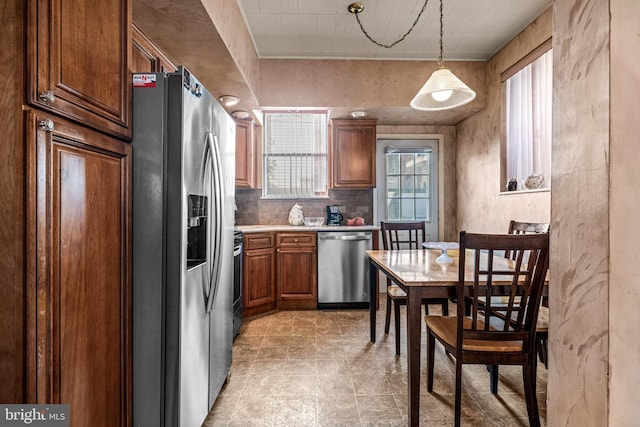 kitchen with stainless steel appliances, light countertops, brown cabinets, hanging light fixtures, and decorative backsplash