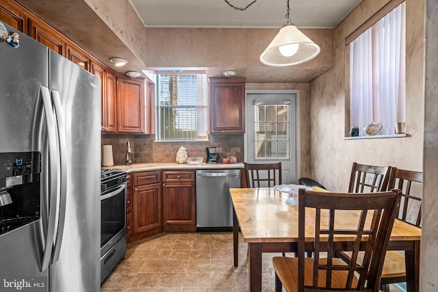 kitchen with stainless steel appliances, light countertops, brown cabinetry, tasteful backsplash, and hanging light fixtures