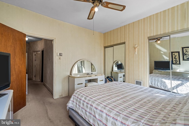 carpeted bedroom with wallpapered walls, ceiling fan, and two closets