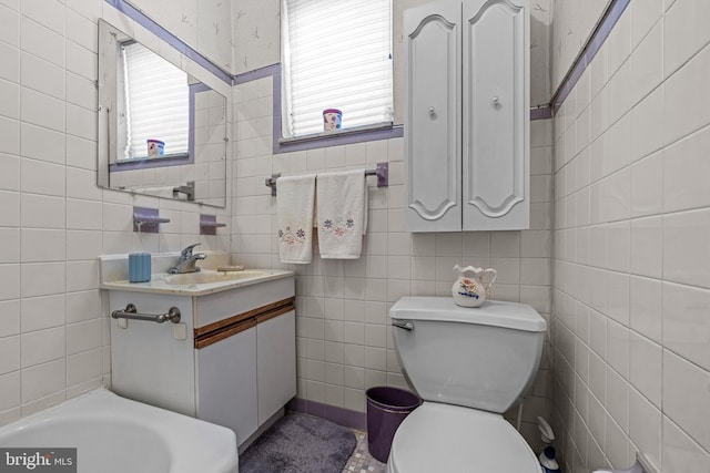bathroom with healthy amount of natural light, toilet, tile walls, and vanity