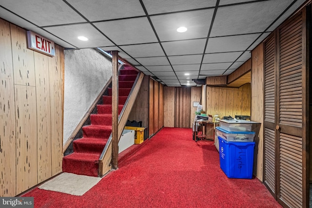 finished basement featuring carpet flooring, wood walls, stairway, a paneled ceiling, and recessed lighting