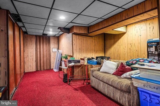 living area featuring carpet flooring, wooden walls, and a drop ceiling