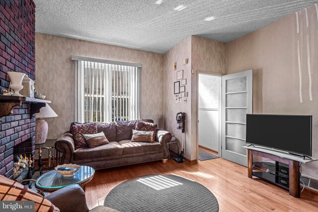 living area featuring wood finished floors, a brick fireplace, and a textured ceiling