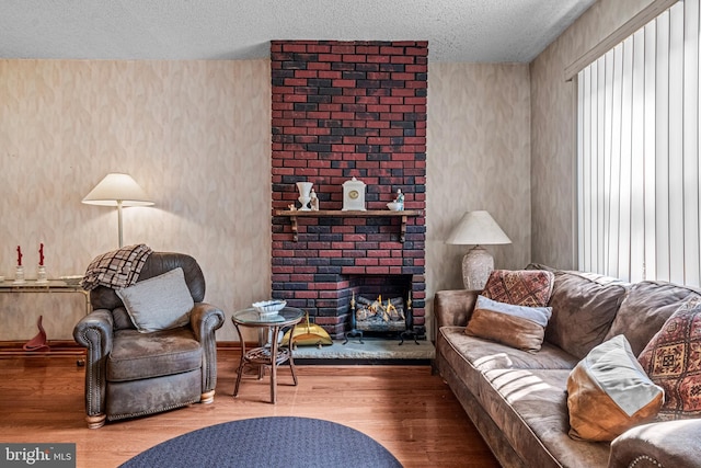 living room featuring a textured ceiling, wood finished floors, and a brick fireplace