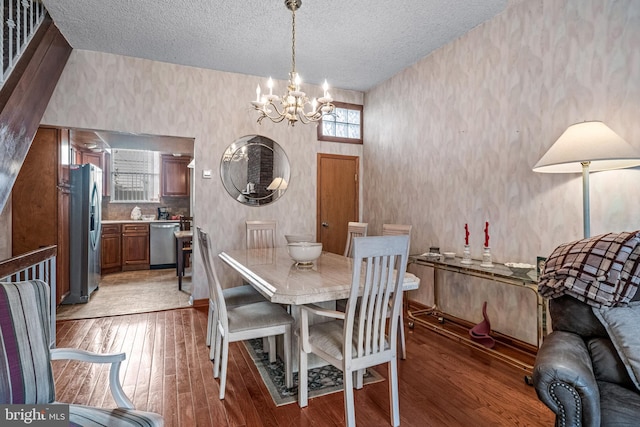 dining area with a chandelier, a textured ceiling, wallpapered walls, and light wood finished floors