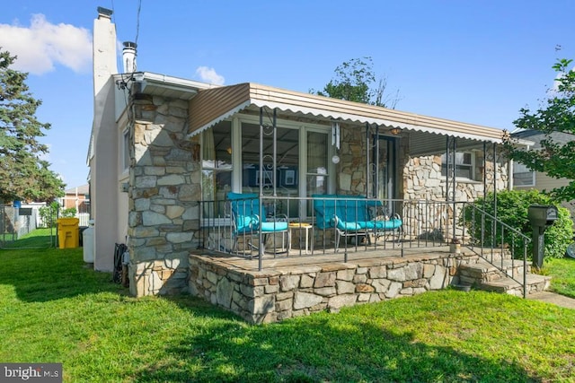 back of property with a yard, stone siding, and a chimney
