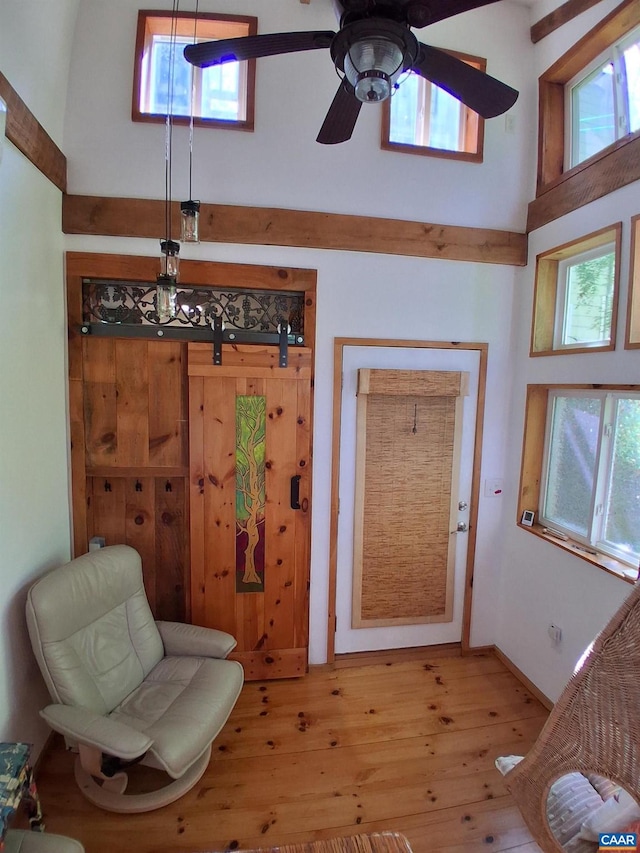 sitting room featuring light wood-style flooring, a towering ceiling, a ceiling fan, and baseboards