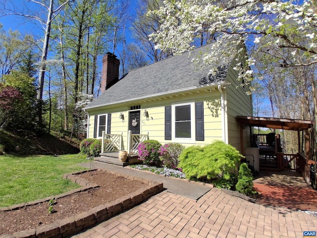 cape cod house featuring a chimney, a front yard, and roof with shingles