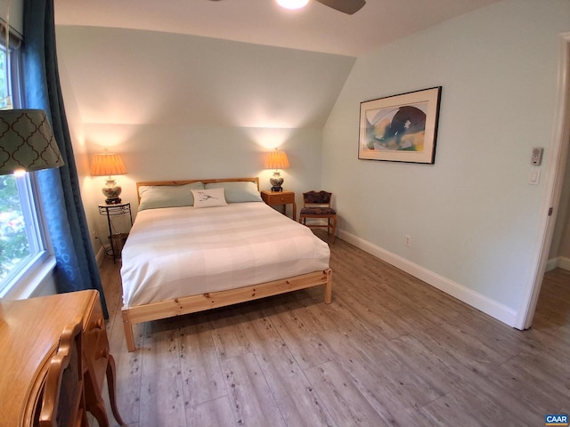 bedroom with wood finished floors, multiple windows, lofted ceiling, and baseboards