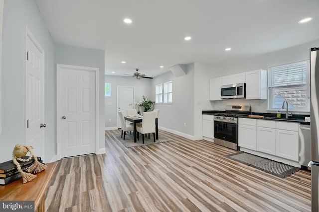 kitchen with appliances with stainless steel finishes, a sink, dark countertops, baseboards, and light wood-style flooring