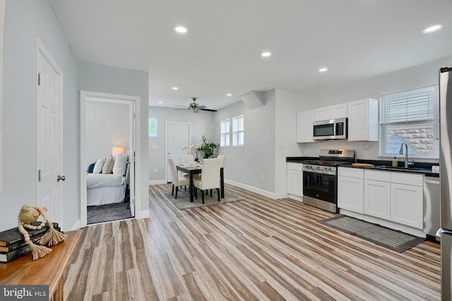 kitchen featuring stainless steel appliances, a sink, dark countertops, baseboards, and white cabinetry