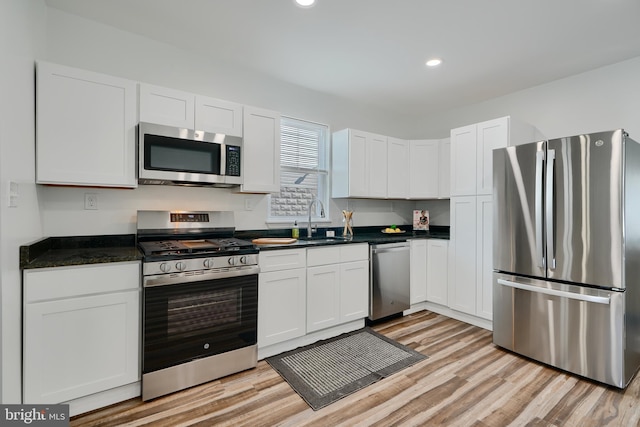 kitchen featuring appliances with stainless steel finishes, a sink, dark countertops, white cabinetry, and light wood-style floors