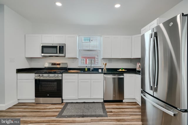 kitchen with appliances with stainless steel finishes, a sink, light wood-type flooring, dark countertops, and recessed lighting