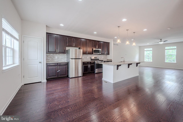 kitchen with appliances with stainless steel finishes, a sink, open floor plan, a breakfast bar, and dark brown cabinets