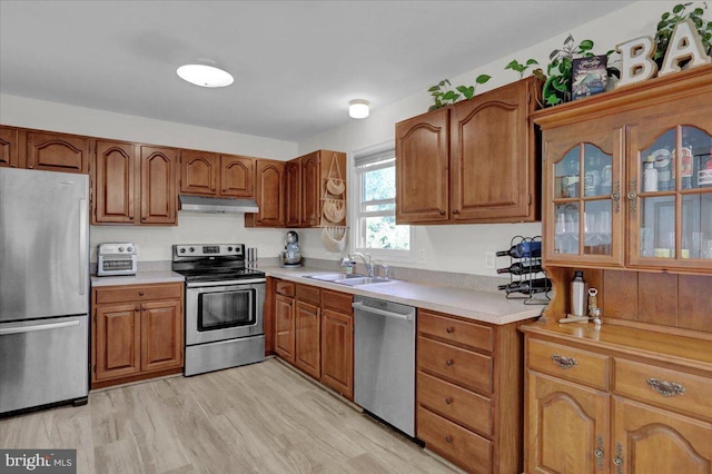 kitchen with stainless steel appliances, under cabinet range hood, a sink, and brown cabinetry
