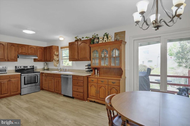 kitchen with appliances with stainless steel finishes, brown cabinetry, a chandelier, under cabinet range hood, and light countertops