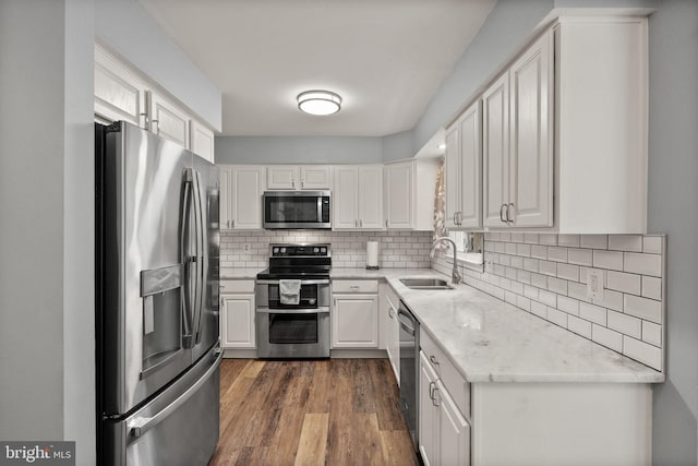 kitchen with stainless steel appliances, a sink, white cabinets, decorative backsplash, and dark wood-style flooring