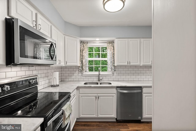 kitchen with appliances with stainless steel finishes, a sink, white cabinetry, light countertops, and dark wood-style flooring