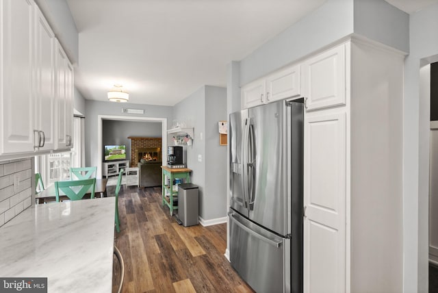 kitchen with stainless steel fridge with ice dispenser, a fireplace, white cabinets, light stone countertops, and dark wood-style floors