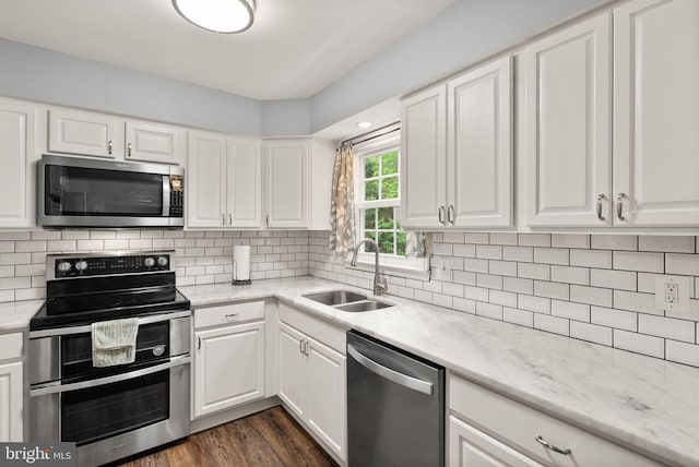 kitchen with appliances with stainless steel finishes, a sink, white cabinetry, dark wood finished floors, and light stone countertops