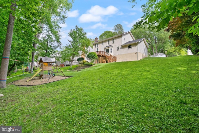 view of green lawn with a playground, stairs, and a wooden deck