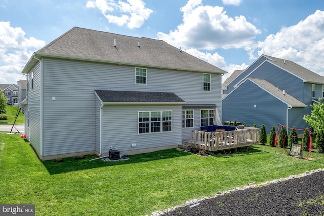 rear view of house featuring a deck, a lawn, and roof with shingles