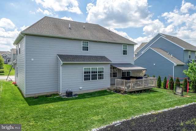 back of property with a wooden deck, a yard, and a shingled roof
