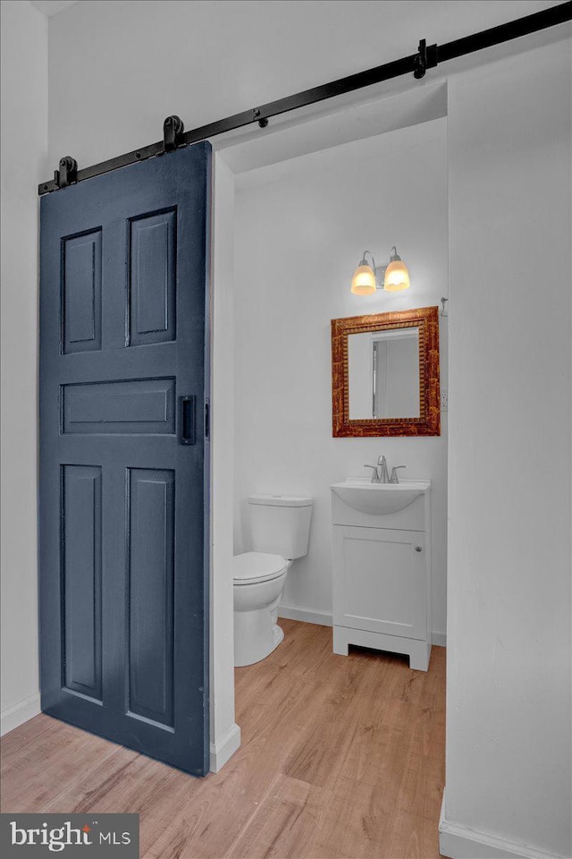 half bathroom featuring toilet, wood finished floors, vanity, and baseboards