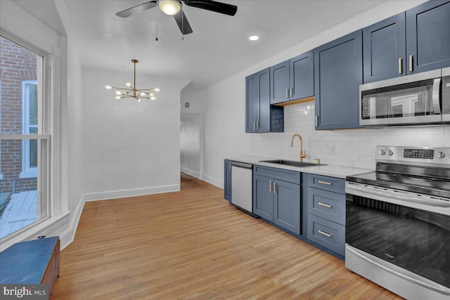 kitchen with appliances with stainless steel finishes, a sink, decorative backsplash, a chandelier, and light wood-style floors
