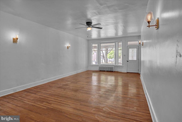 unfurnished living room featuring radiator heating unit, ceiling fan, wood finished floors, and baseboards
