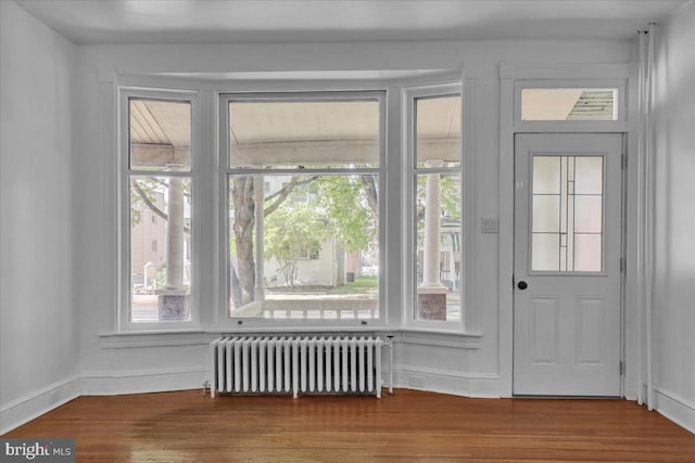 doorway to outside with radiator, wood finished floors, and baseboards