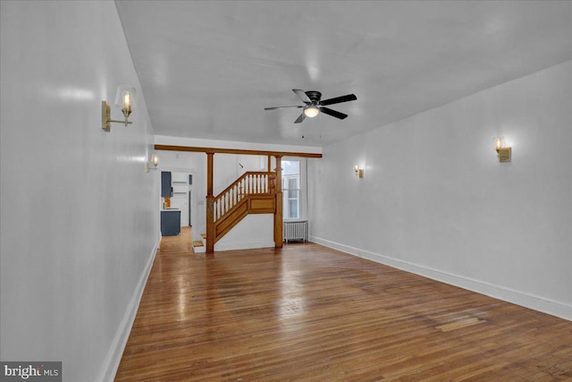 unfurnished living room with stairs, radiator heating unit, baseboards, and wood finished floors