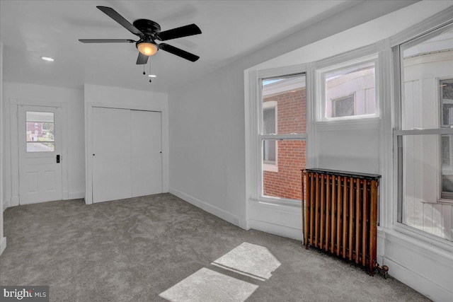 unfurnished living room featuring carpet floors, radiator heating unit, and a ceiling fan