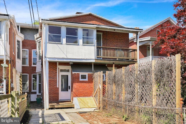 rear view of property featuring brick siding, a balcony, and fence