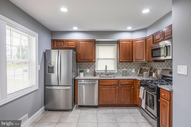 kitchen with appliances with stainless steel finishes, a sink, tasteful backsplash, light stone countertops, and plenty of natural light